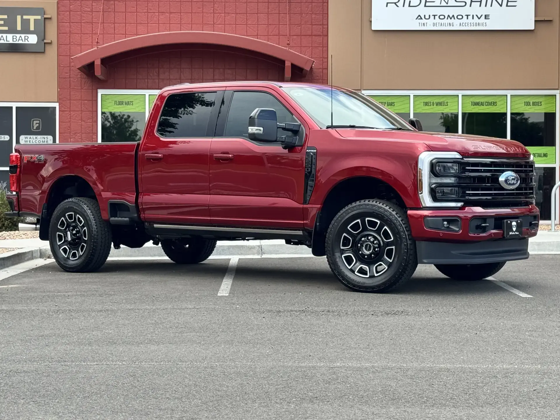A red Ford F-250 Super Duty parked outside the Ride N' Shine storefront, beside window signs for floor mats, step bars, tires and wheels, tonneau covers, and tool boxes