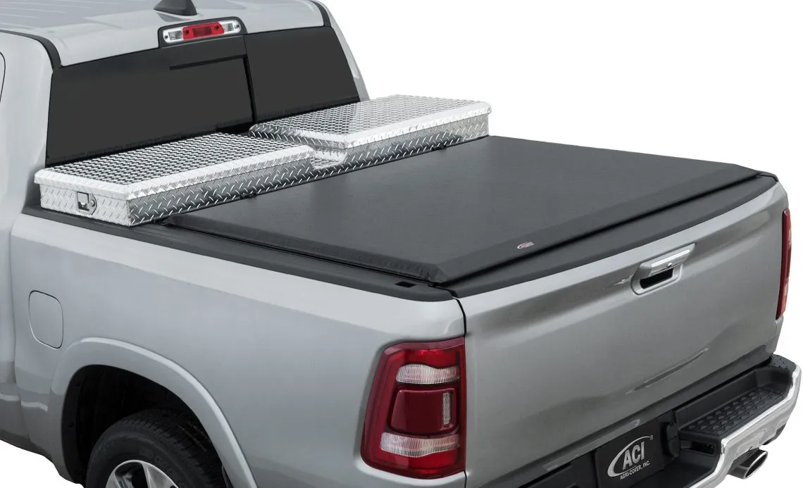A silver pickup with a diamond-plate aluminum crossover tool box mounted behind the cab, paired with a soft roll-up tonneau cover