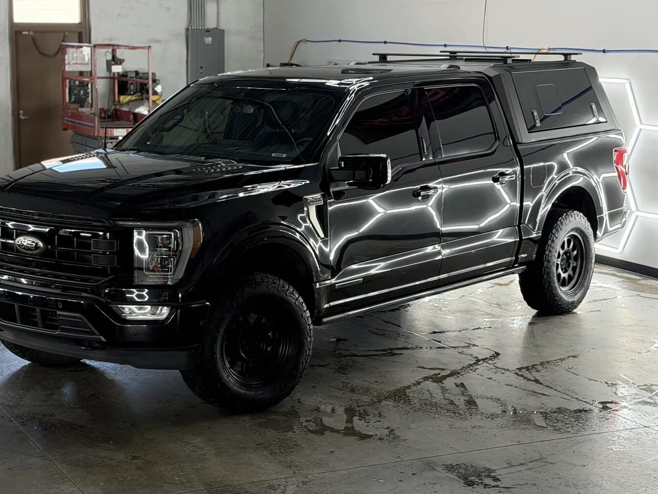 A black Ford F-150 with a camper shell under the studio's hexagon lights