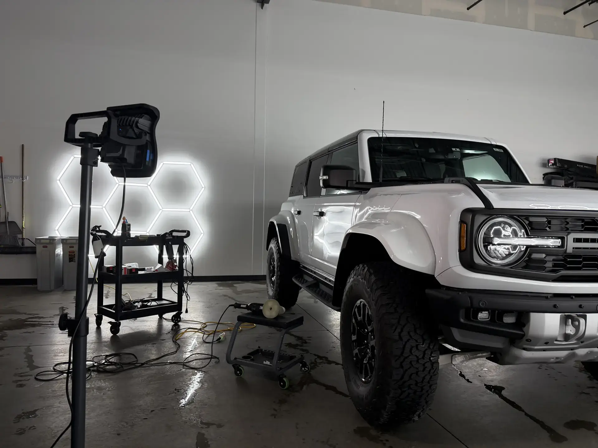 A white Ford Bronco Raptor on the studio floor beside a polisher and an inspection light
