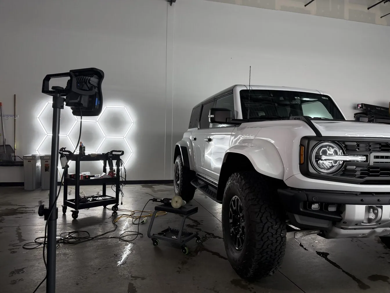 A white Ford Bronco Raptor beside a polisher and an inspection light during a detail