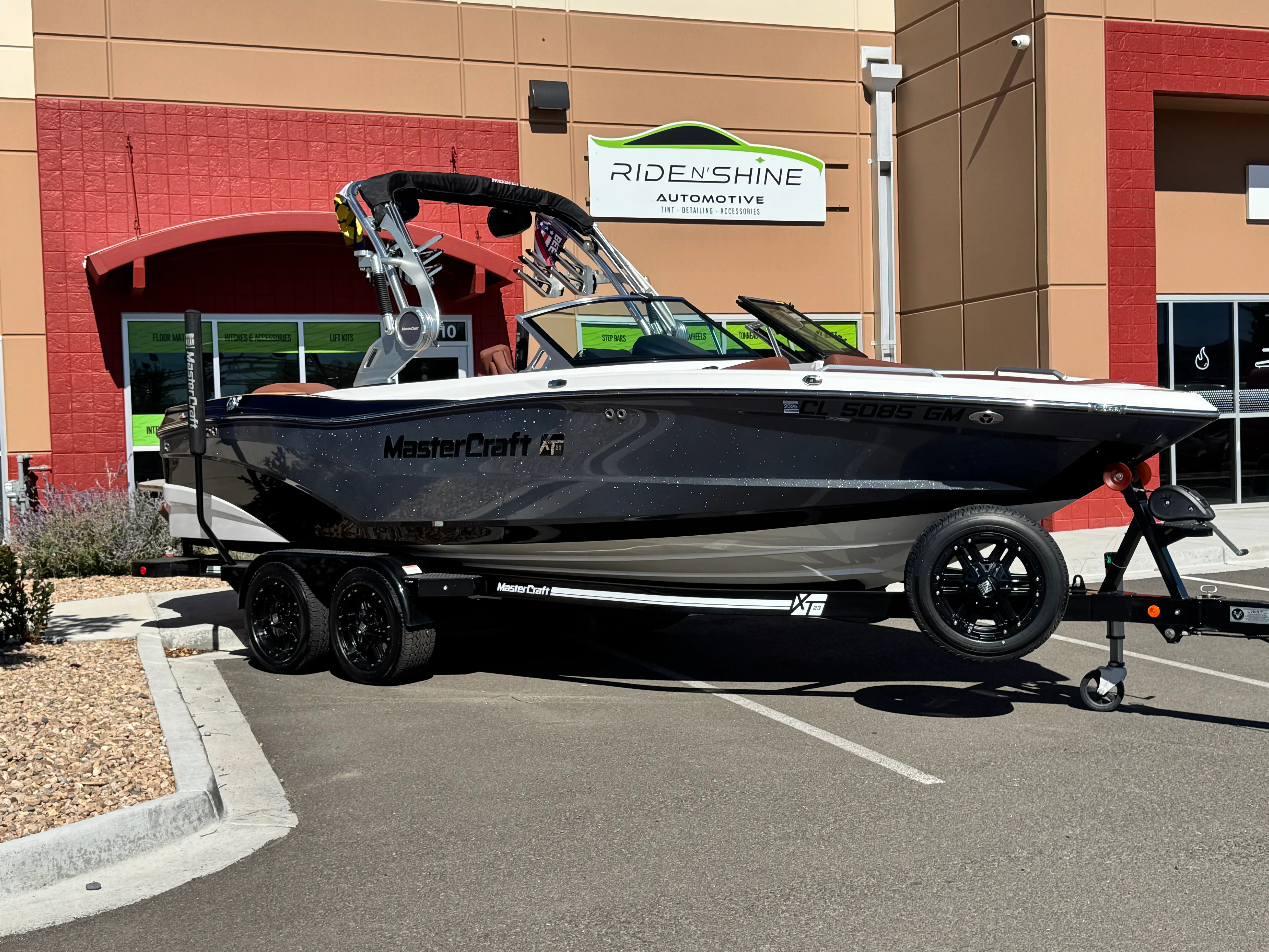 A black MasterCraft XT23 on its trailer outside the Ride N' Shine storefront, its metalflake hull polished to a gloss