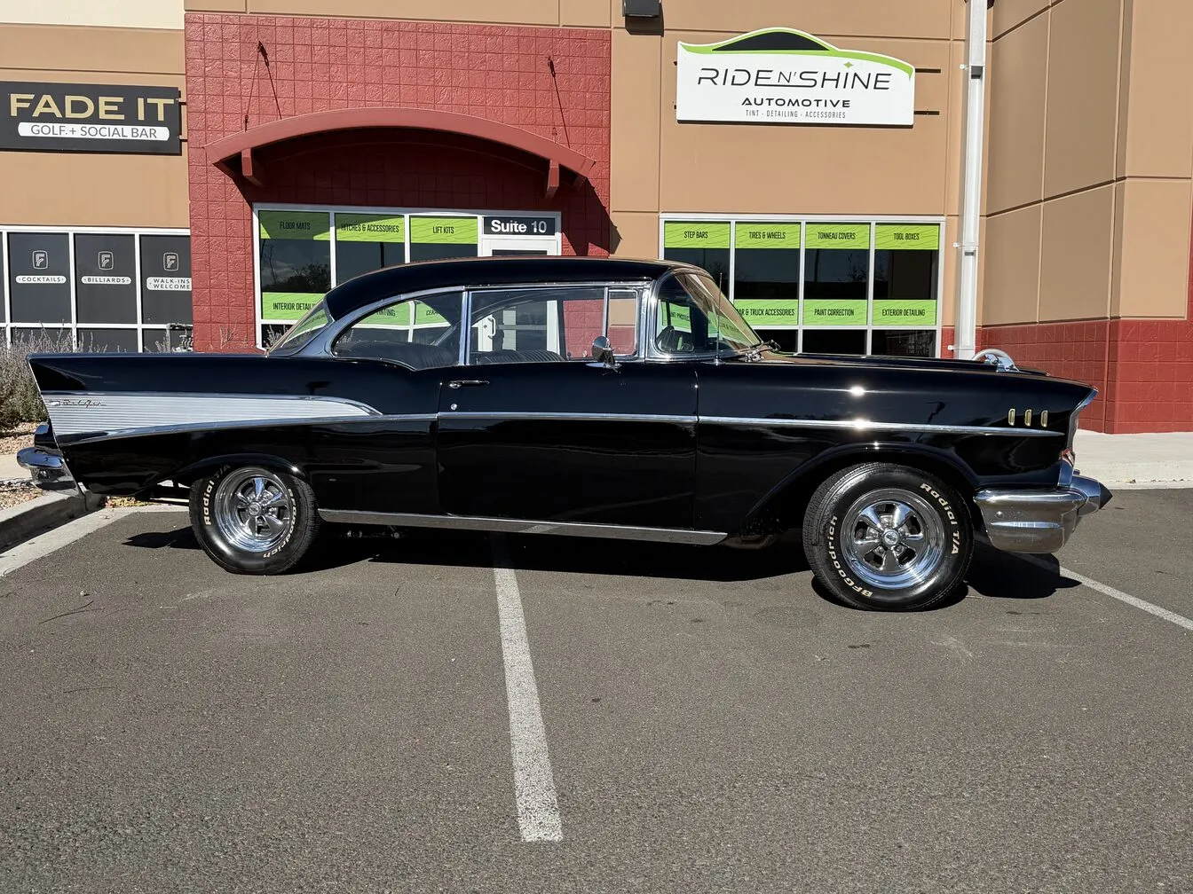 A black 1957 Chevrolet Bel Air parked outside the Ride N' Shine storefront