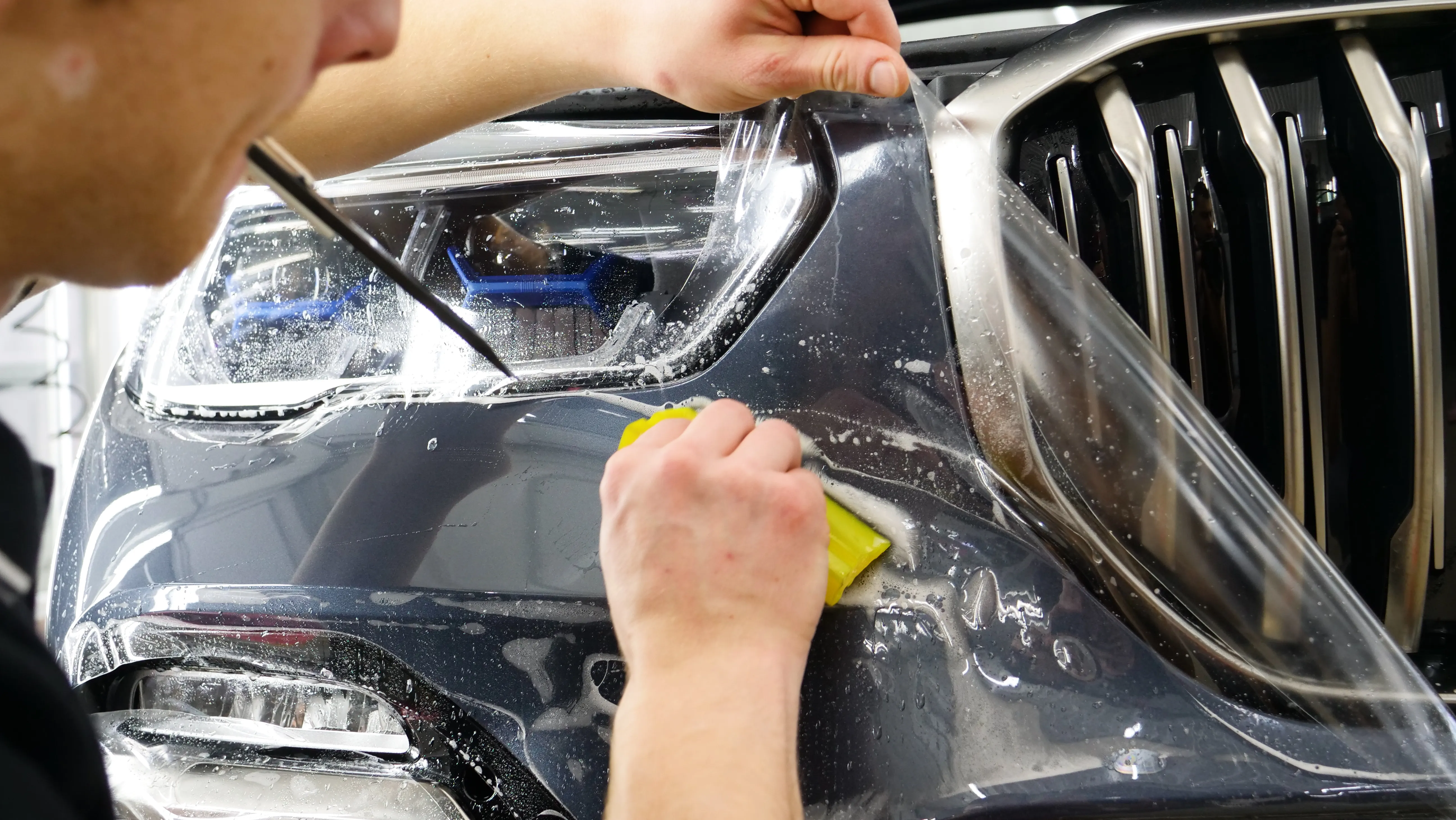 An installer squeegeeing paint protection film onto a headlight and front bumper
