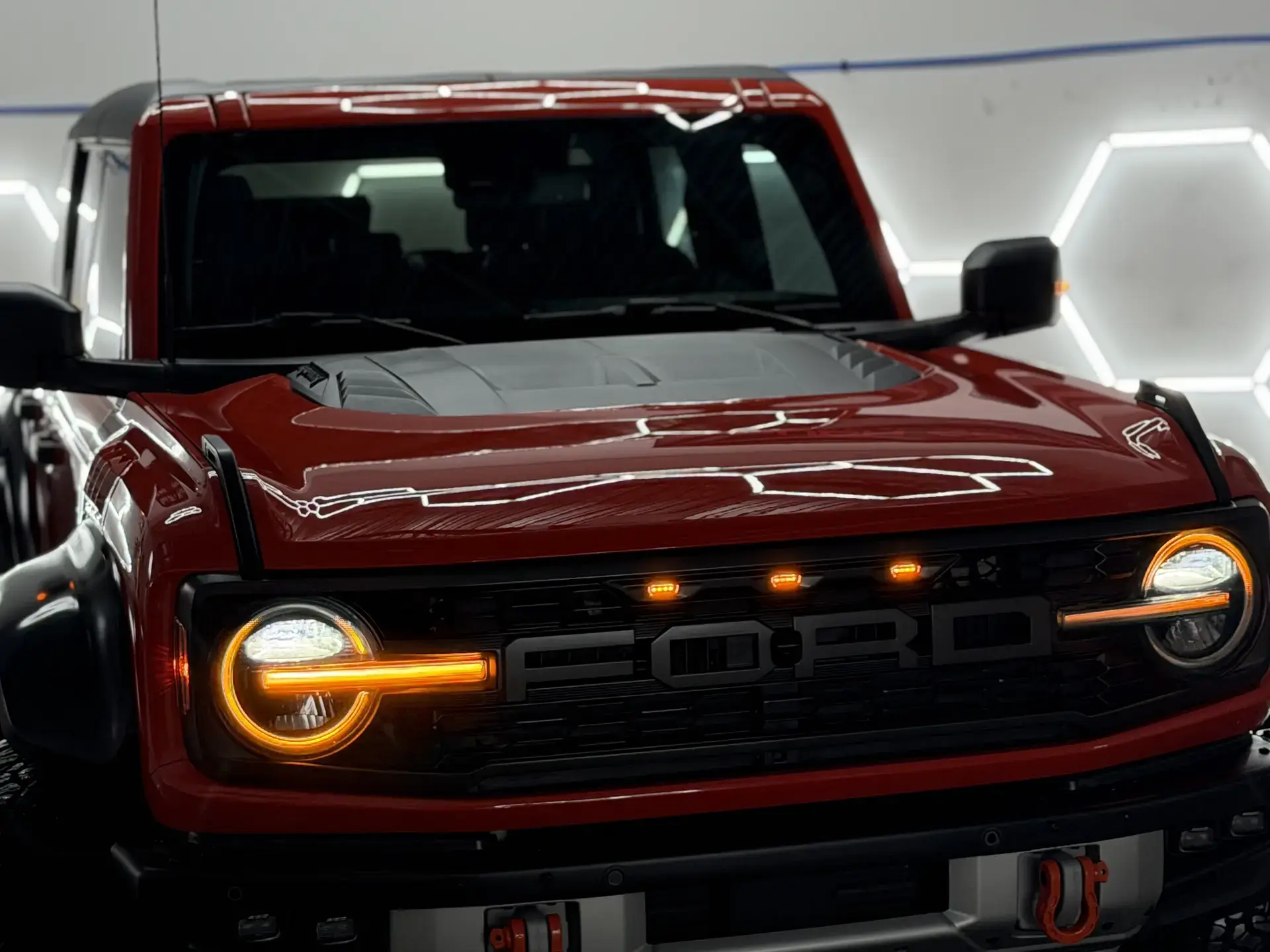The front end of a red Ford Bronco Raptor under the studio's hexagon lights