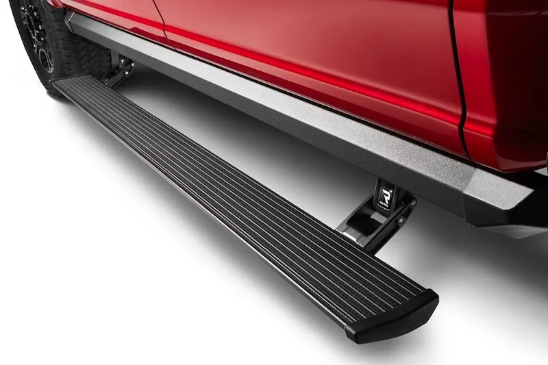 A black AMP Research PowerStep running board extended below the cab of a red pickup