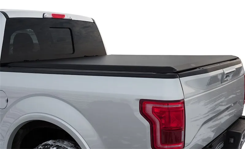 A black soft roll-up tonneau cover closed over the bed of a white Ford F-150