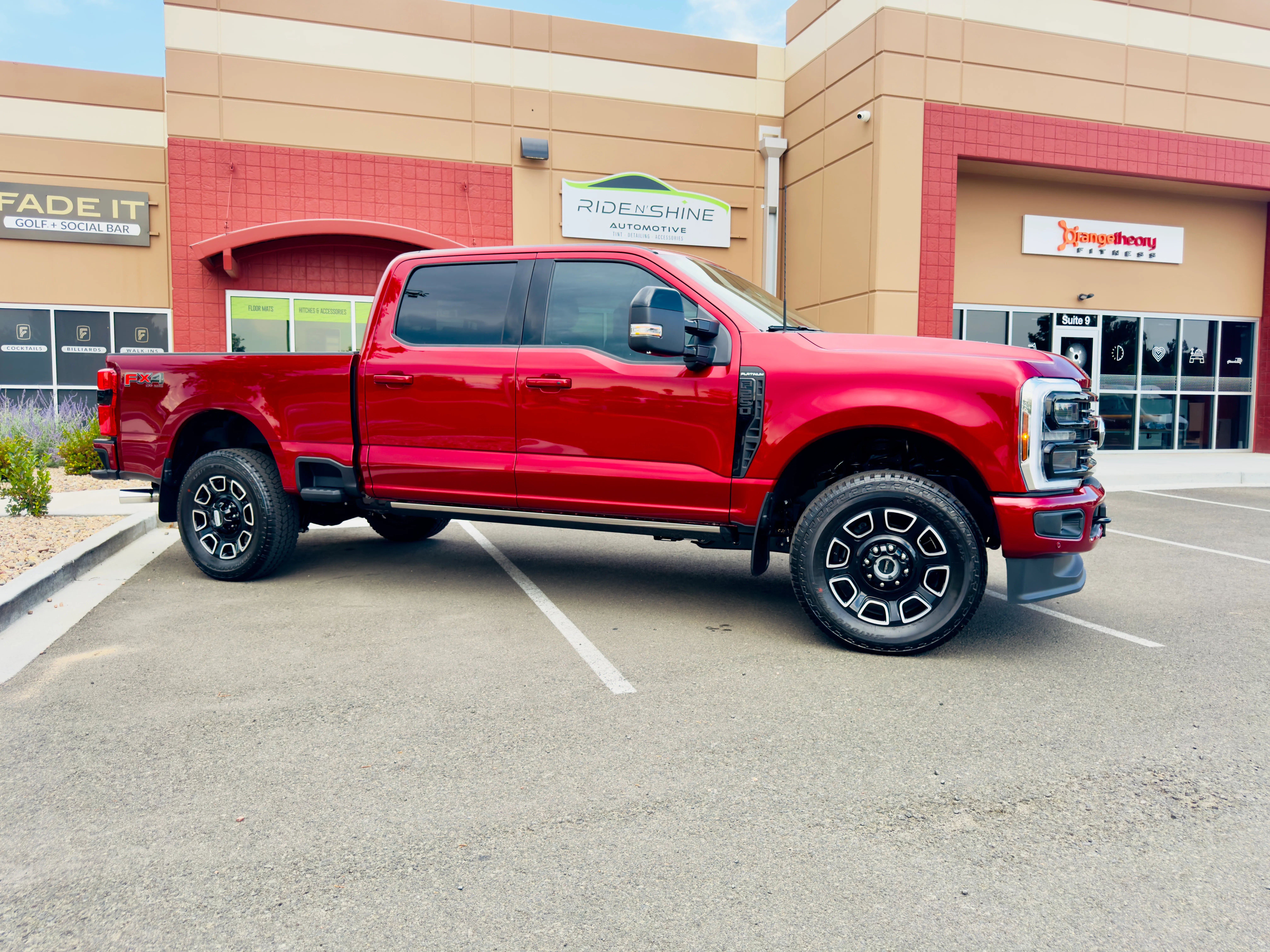 A red Ford F-250 Super Duty with tinted windows parked outside the Ride N' Shine storefront