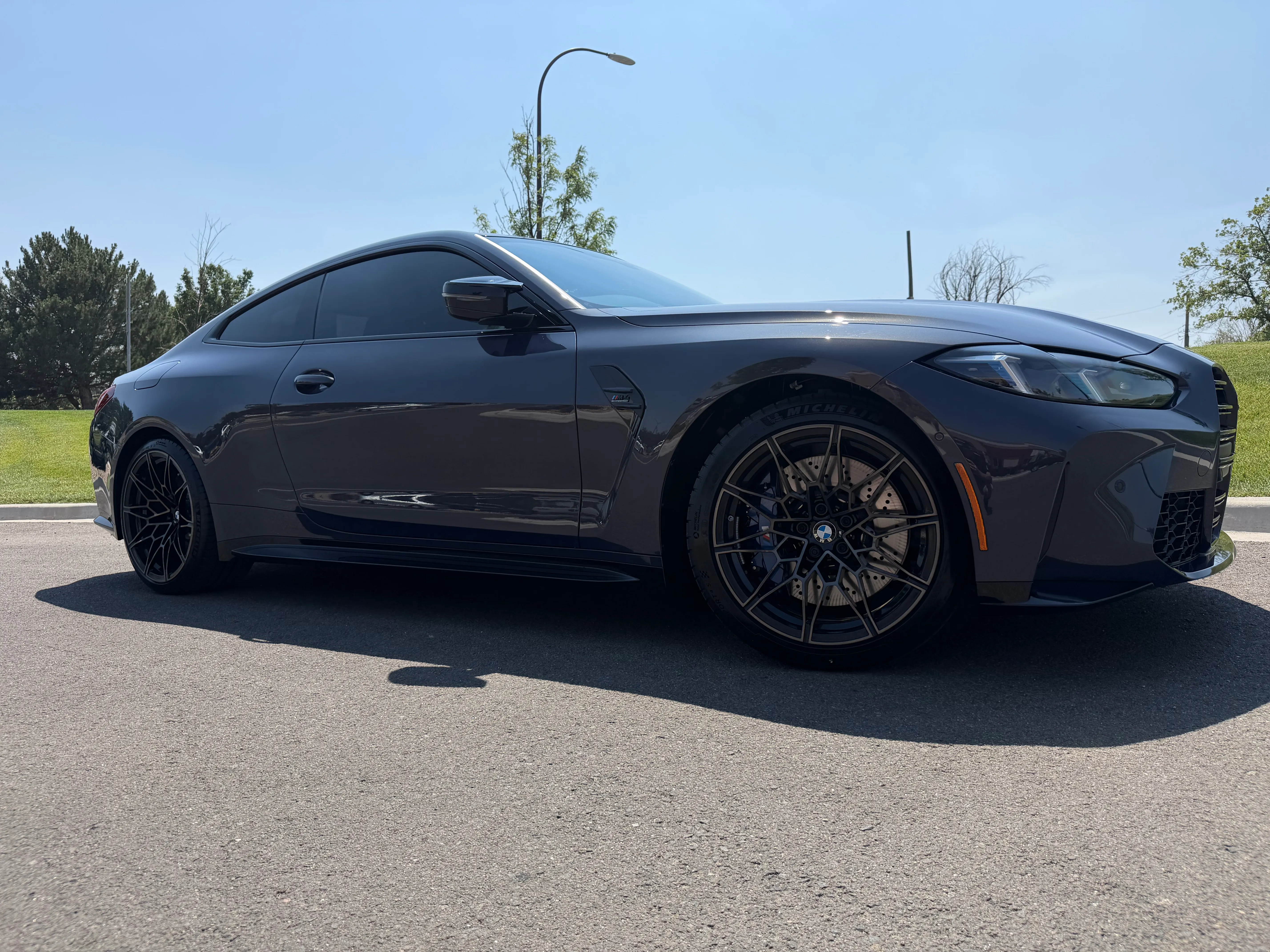 A dark grey BMW M3 with tinted windows parked on a sunny street