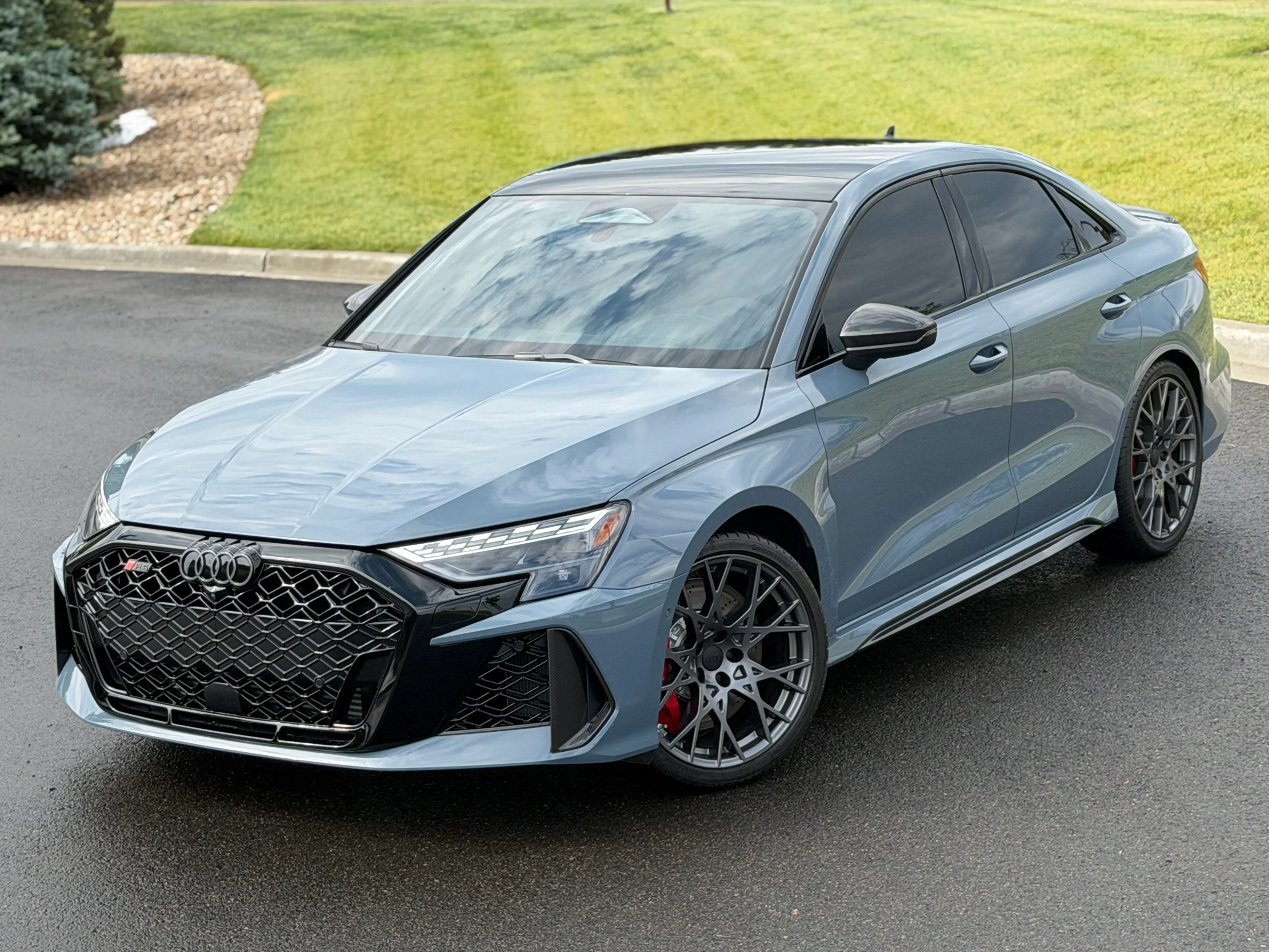 A grey-blue Audi RS3 sedan with tinted windows parked on wet pavement