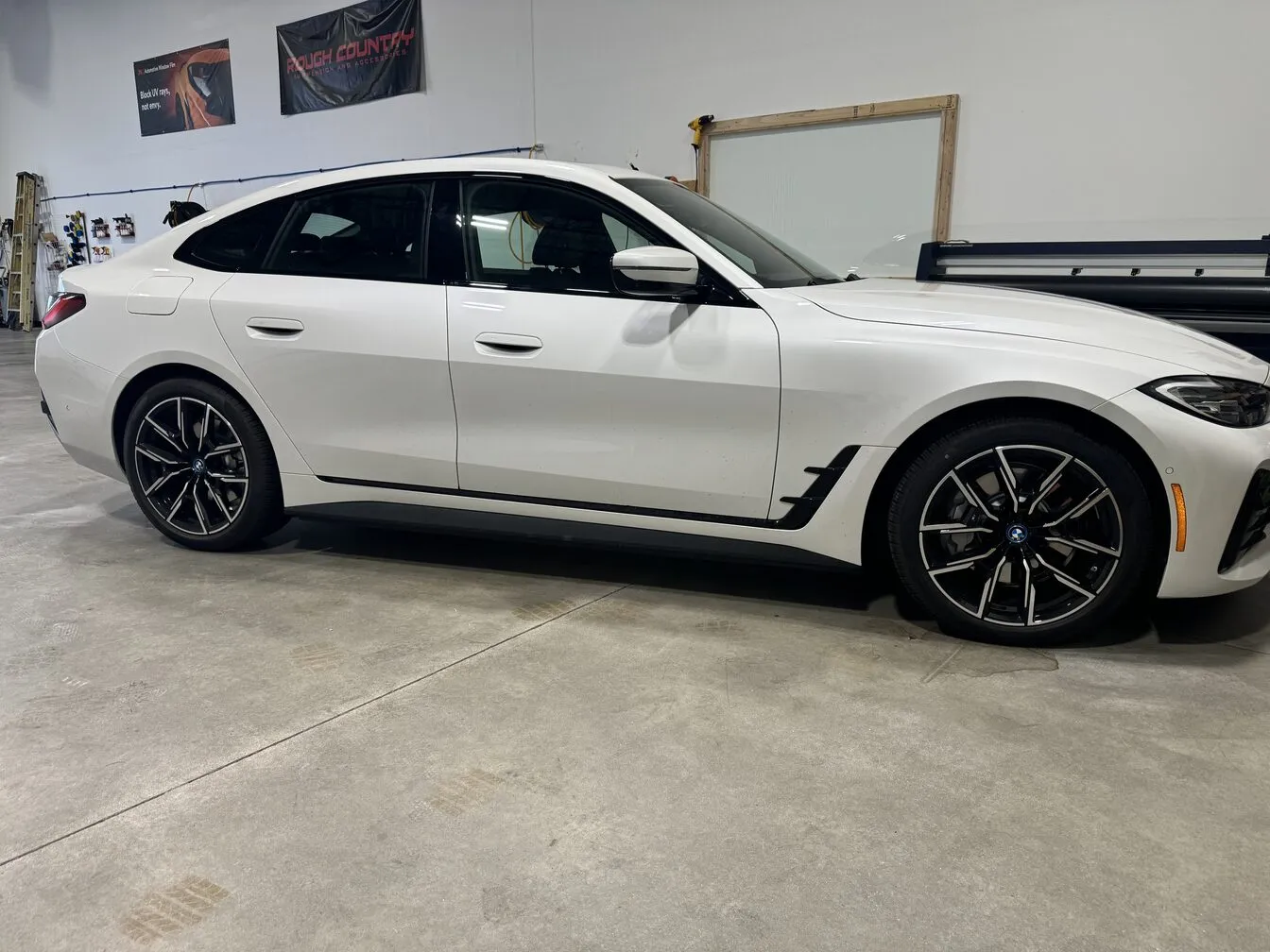 A white BMW 4 Series Gran Coupe parked inside the studio beside a glass work panel